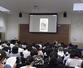 多くの参加者と講師。スクリーンには昔話の参考資料が映し出されている。