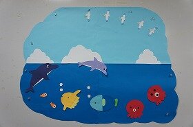真っ青な空を背景に、イルカやマンボウ、タコたちが楽しそうに飛び跳ねたり泳いだりしている壁面装飾です