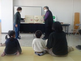 大型絵本『おしくら・まんじゅう』を親子で見ている様子。