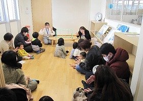 写真1　おはなしのへやで「はじまるよ」の手遊びをしている様子。