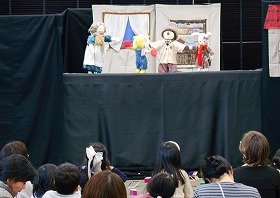 写真3：人形劇「おばあさんのたんじょうび」の写真。おばあさんの家の中で、左からおばあさん、きつね、くま、うさぎが立っている。