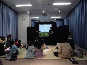 大型絵本を持つ2人の女性とそれを見つめる親子。