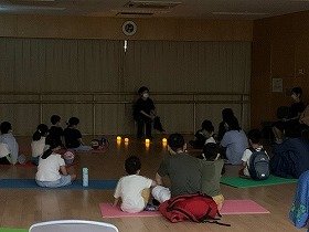 暗い部屋でおはなしをする演者と、聴いている親子達