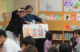 大型絵本を手話で読んでいる人とページをめくっている人が写っています。