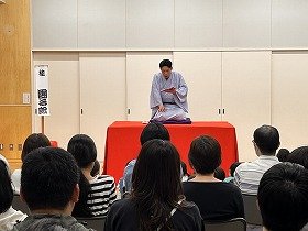 写真2　本を読む仕草の表現について説明する桂團治郎さんの写真です。