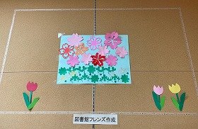 朱色や濃いピンクや薄いピンクで作った桜の花びらの下にクローバーが咲いている。赤とピンクと黄色のチューリップも咲いている。