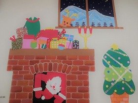 写真　暖炉の上にプレゼント。サンタが暖炉の中から覗いている。トナカイは窓から覗いている。