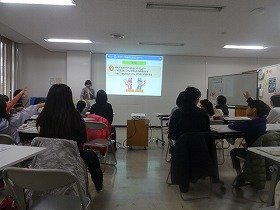 写真　講師が出したクイズに手を挙げて答えている子供たちと同伴の保護者。