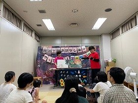 画像1　大型絵本『めっきらもっきらどおんどん』の読み聞かせを親子で聞いている様子。