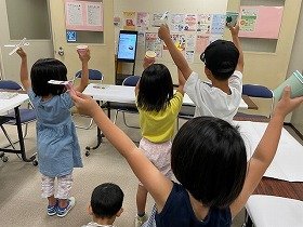 写真2　「かえるジャンプ」と「紙コプター」の完成品を持って万歳している参加者