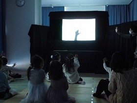 影絵のスクリーンに映し出される手にあわせて、手を上げる子どもたち。