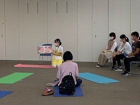 YAサポーターの学生が親子に向かって絵本を読む様子。