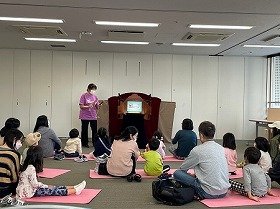 拍子木を叩く演者と紙芝居を見ている親子の様子。