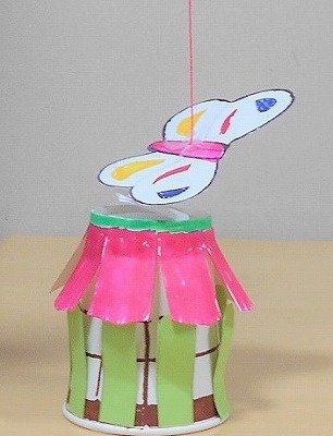 紙コップで作った花の上をちょうちょが飛んでいる写真。